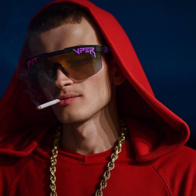 A young man wearing a red hoodie, gold chain, and futuristic sunglasses with 'NFER' text smokes a cigarette against a dark blue background.