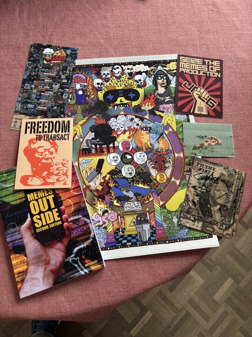 A collection of 'MEMES' zines and printed artwork laid out on a pinkish surface, including titles like 'FREEDOM TO TRANSACT', 'SEIZE THE MEANS OF PRODUCTION', 'FILTHY PLAY', and 'MEMES OUT SIDE SECURE EDITION'.