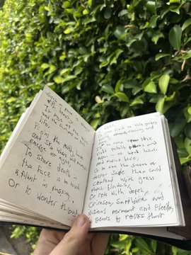 A close-up of a hand holding an open notebook filled with handwritten text and poetry.