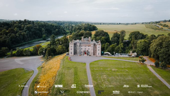 An aerial view of a large castle estate with expansive green grounds, overlaid with multiple sponsor logos including Attribute, SKYROSE, Jet, Seeker, Jito, and others.