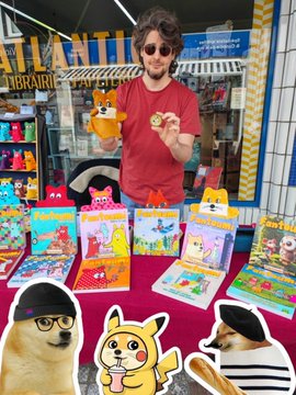 A vendor at a market stall surrounded by colorful prints and plush toys, with cutouts of Shiba Inus and Pikachu in the foreground.