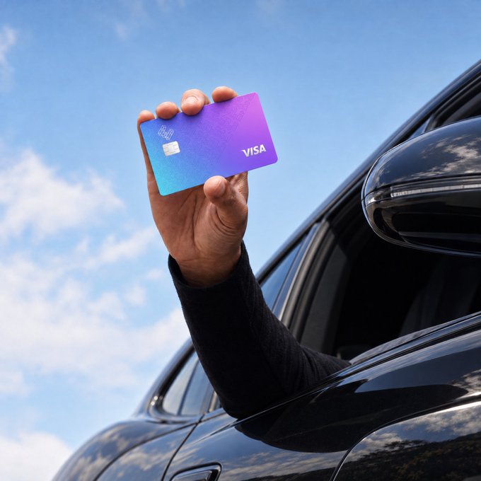 A hand extends out of the window of a black car, holding up a purple and blue gradient Visa card toward a partly cloudy blue sky, visually representing the post's claim about using a crypto-linked EtherFi Cash card to purchase a car without selling crypto, with the card symbolizing the payment method that enabled 36 such car purchases in August, including one over $120K.