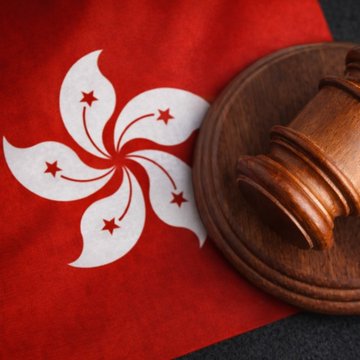 A wooden judge's gavel rests atop the Hong Kong flag, featuring its iconic white bauhinia flower emblem with red stars, symbolizing the city's potential emergence as a leading crypto hub following the CLARITY Act delay.