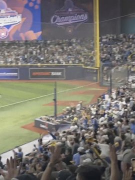 A packed baseball stadium is shown with fans celebrating near the foul pole and outfield. A banner reads “CHAMPIONS,” while the accompanying post explains that the scoreboard mistakenly announced the Milwaukee Brewers as World Series champions during Game 4, even though they lost to Tampa Bay and still lead the series 3–1.