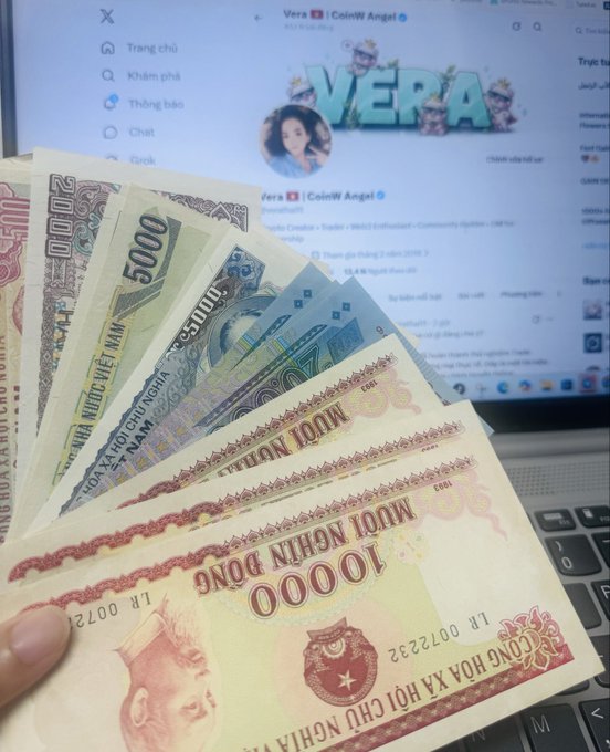 A hand holds a fan of Vietnamese dong banknotes (including 10,000 and 5,000 denominations) in front of a laptop displaying the X (Twitter) profile of 'Vera | Coin88 Angel' with 'VERA' branding.
