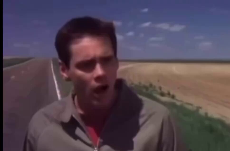 The image features a man standing on an asphalt road, which appears to be a two-lane highway. He has his mouth open as if speaking or making a face, adding a sense of emotion or surprise to the scene. The background consists of a landscape with green grass and a large body of water, contributing to the overall mood of the photograph. However, there is no clear connection between the man's appearance in the photo and the post about buying Litecoin for $400.