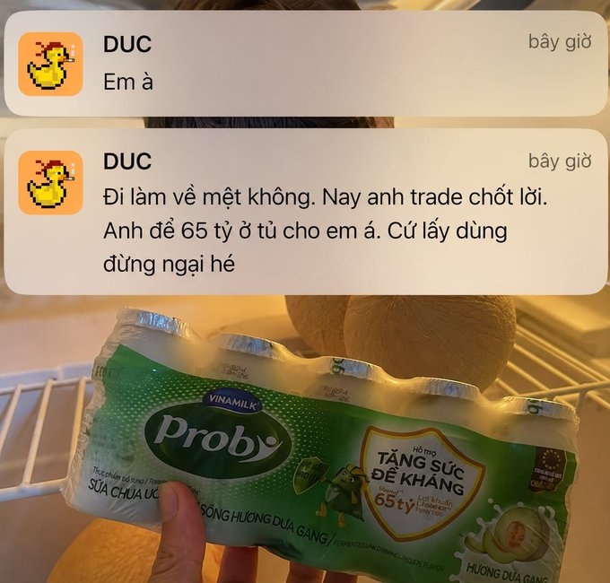A hand holds a pack of Vinamilk Probi yogurt featuring green packaging that advertises "65 tỷ lợi khuẩn" (65 billion probiotics) and "Hương Dưa Gang" (honeydew melon flavor), while a messenger chat overlay shows "DUC" sending messages about trading profits and gifting 65 billion to his loved one—cleverly tying the yogurt's "65 tỷ" probiotic claim to the trader's brag about his 65 tỷ VND trading gains.