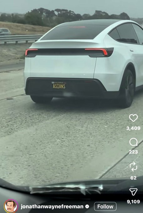 A white Tesla is parked on a road shoulder, displaying a California license plate reading "ASTANS" that cleverly reads "ASS-TANS." The image supports the post's joke about free money at "0%" interest, mocking the obscuring of identifiers on personalized plates.