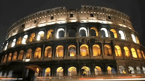 The image features a large, circular building with many arches at night. The building has a unique architectural design that stands out against the dark sky. In the surrounding area, there are several people walking around or standing near the building, possibly admiring its beauty and discussing its details.