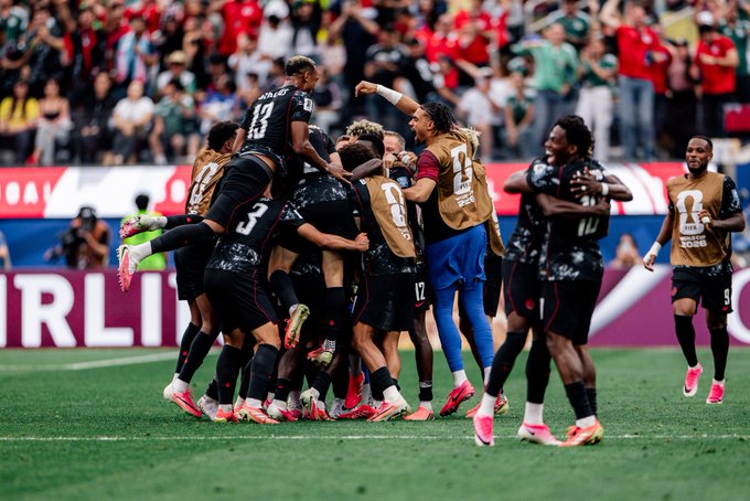 AC Milan players wearing black and gold kits, including numbers 23, 8, 12, and 19, celebrate together on the pitch while a teammate in a gold training bib runs to join them, perfectly embodying the pride and unity behind the "National treasures" sentiment as the team shares a triumphant group hug after what appears to be a significant victory.