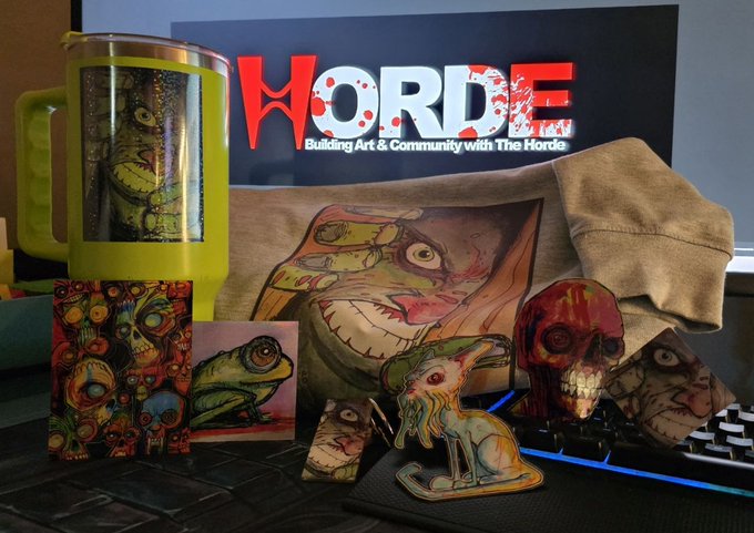 An assortment of Horde-themed merchandise is displayed including a yellow travel mug, stickers, a t-shirt with zombie art, and a skull-shaped cup, with a 'HORDE - Building Art & Community with The Horde' sign.