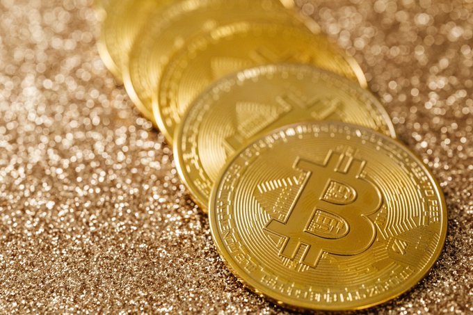A row of physical Bitcoin tokens fanned out on a glittering gold surface, with the iconic "₿" symbol and the words "BITCOIN DIGITAL" engraved on their faces. The image visually echoes the post's comparison between gold's ancient role as a store of value and Bitcoin's modern ambition to become "digital gold."