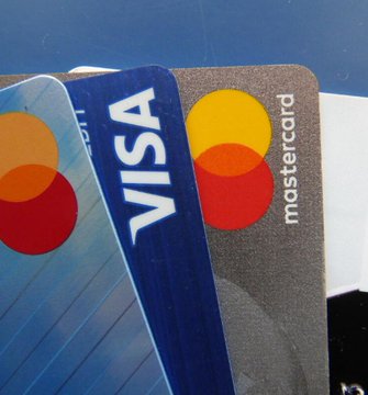 Two overlapping credit cards—a blue Visa and a MasterCard with their recognizable logos—are displayed against a dark background, visually representing the article's topic of purchasing meme coins like WIF with Robinhood and Fomo using credit cards without KYC verification, which has prompted JPMorgan to ask Visa to investigate.
