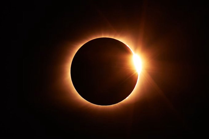 A solar eclipse showing the moon blocking the sun, with a brilliant burst of light—resembling the "diamond ring" effect—emerging from behind the dark lunar silhouette. This celestial alignment of Sun (Sol), Earth (Terra), and Moon (Luna) visually embodies the cosmic trinity described in the caption.