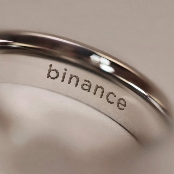 A silver wedding band engraved with the word "binance" is shown in close-up, symbolizing a lasting commitment to the cryptocurrency platform. The engraving replaces a traditional name or date, humorously framing brand loyalty as a marital vow.