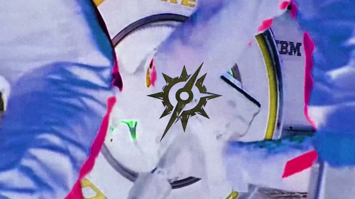 The image features a close-up of two people's hands, with one hand holding a white object that has a black star symbol on it. The other hand holds a blue object with a red stripe running down its side. The background appears to be a grayish color and is blurred out, making the focus on the hands and objects more prominent in the image.