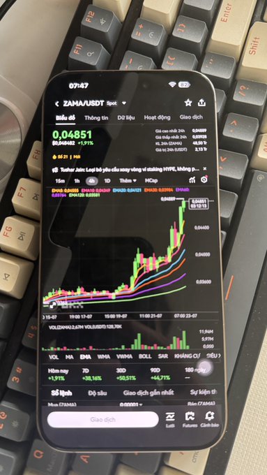 A smartphone displays a Vietnamese stock trading app showing ZAWASAUDOT (ZMS) at 0.04851, up +1.91%, with a candlestick chart and volume indicators, resting on a mechanical keyboard.