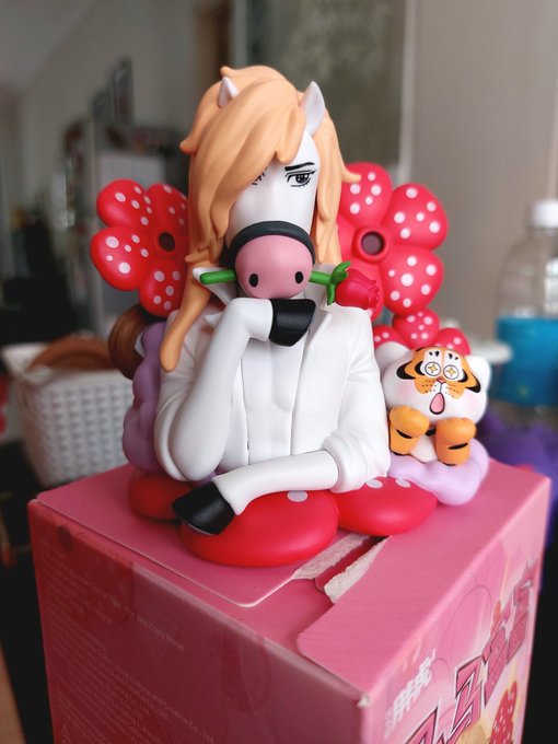 A vinyl figure of an anime character with orange hair, cat ears, and a white outfit, sitting on a pink box alongside a small red mushroom-like mascot.