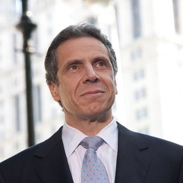 The image features a man dressed in a suit and tie standing outside of an office building. The man appears to be looking up at something or someone above him, possibly a colleague or a passerby. The photo captures his attention and suggests that he is engaged in a conversation or observing something interesting happening around him.