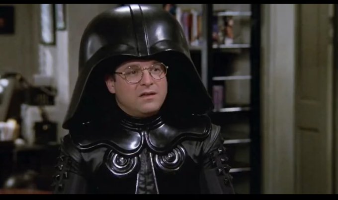 A still from the movie Spaceballs showing the character Dark Helmet, played by Rick Moranis, wearing his iconic oversized black helmet and costume.