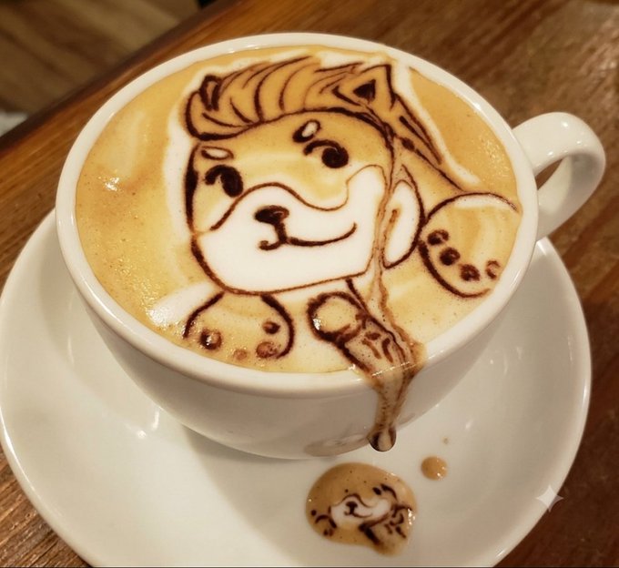 A latté art image of a cute puppy with a spill forming a smaller puddle puppy on the saucer, perfect for the "Who wants some coffee?" caption inviting viewers to enjoy a delightful cup of coffee.