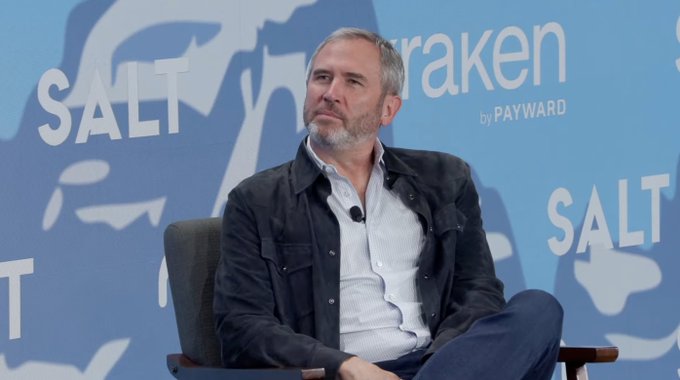 Brad Garlinghouse, CEO of Ripple, sits on a panel at the Wyoming Blockchain Symposium, with "SALT" and "kraken by PAYWARD" logos visible in the background, appearing thoughtful as he discusses crypto regulation and Ripple's compliance efforts.