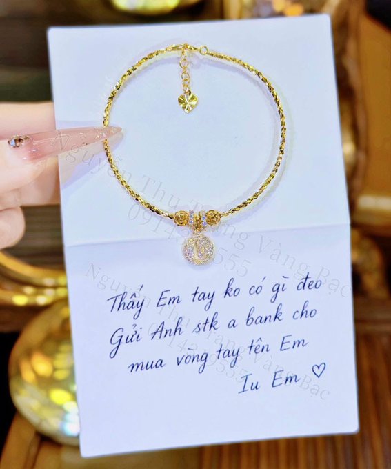 A hand holds a white card displaying a gold bracelet with a crystal pendant, accompanied by a Vietnamese message asking the recipient to buy a bracelet.