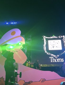 A live concert or nightclub scene featuring a large illuminated astronaut mascot head on the left, with an LED screen displaying the word 'Thorns' on the right.