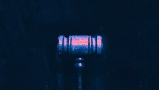 A dark, atmospheric image of a wooden judge's gavel illuminated by a blue and pink light against a black background.