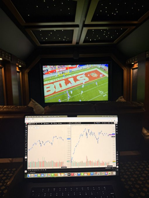 A laptop displaying stock charts sits in front of a large screen broadcasting a Buffalo Bills football game, all under a ceiling designed to look like a starry sky—capturing the perfect blend of football season and active market watching for peak Q4 vibes.