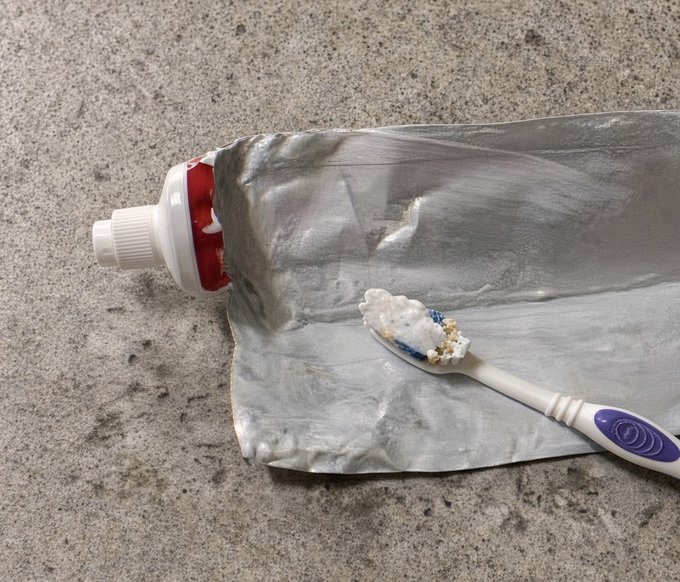 A used tube of toothpaste lies flat on a speckled countertop with a toothbrush bearing leftover paste resting on top, humorously representing "Thank Ethereum" by likening its empty, tube-flattened state to a strip-mined cryptocurrency—depleted and squeezed dry of value.