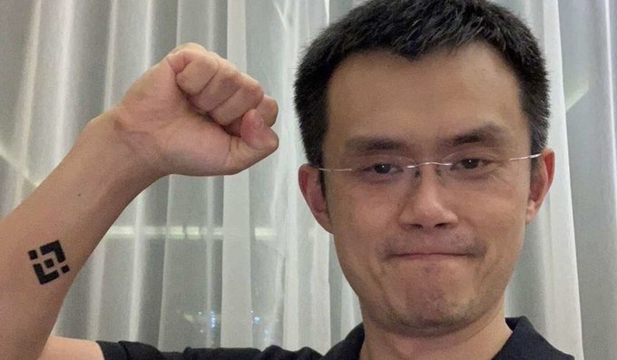 Changpeng Zhao, founder of Binance, raises his fist while displaying a small Binance (BNB) logo tattooed on his forearm, embodying the conviction behind the post's lesson about bold crypto investment.