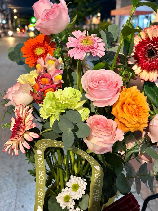 A colorful bouquet of roses, gerbera daisies, and other flowers is wrapped with a ribbon repeatedly printed “JUST FOR YOU.”