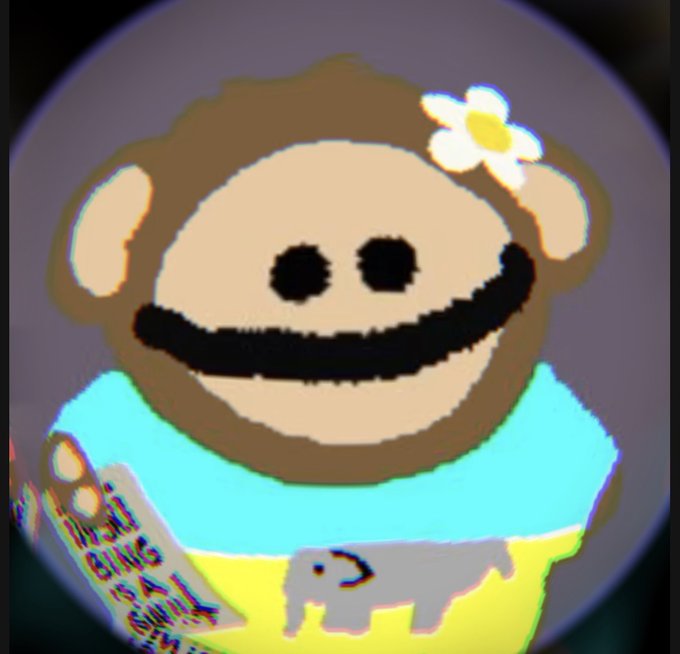 A blurry, distorted cartoon character resembling a brown monkey or bear with a flower on its head, wearing a yellow shirt and a blue bib.
