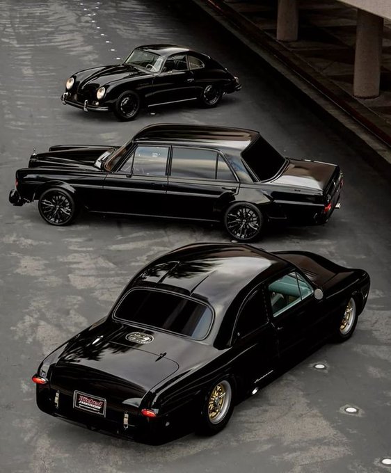Three glossy black classic cars, including a vintage Porsche 356 and two modified sedans, are parked on a concrete surface.