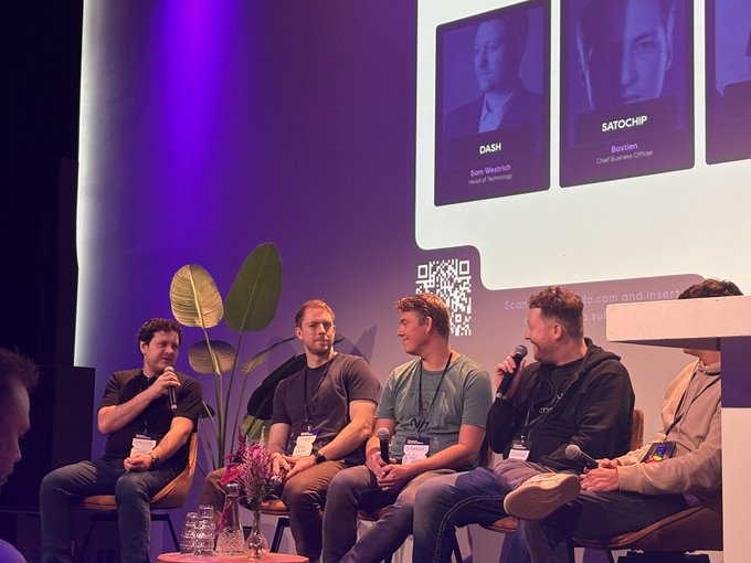 A panel discussion at a tech/crypto conference with five men seated on stage; a screen behind them displays headshots labeled 'DASH' (Sam Wesnitch, Head of Technology) and 'SATOCHIP' (Boeren, Chief Business Officer) alongside a QR code.