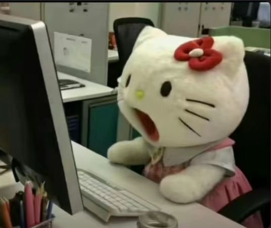 A Hello Kitty plush toy sits at an office desk in front of a computer monitor and keyboard, with its mouth open in an apparent yell of frustration.