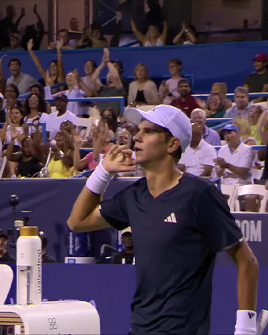 A tennis player wearing an Adidas shirt and white cap blows a kiss to a cheering crowd while holding up his hand in a gesture, with a "Waterdrop" branded water bottle visible on the bench beside him. The image relates to the post's claim that he "holds $TBB" (likely a gesture or symbol) which supposedly contributed to winning the point.