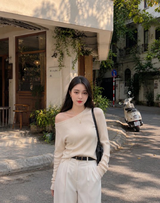 A young woman poses on a quiet street in a beige off-shoulder sweater and white trousers, with a vintage scooter and café in the background. The relaxed, stylish afternoon vibe fits the post's upbeat "Good Morning" energy — a chic, casual look to power through the final workday of the week.