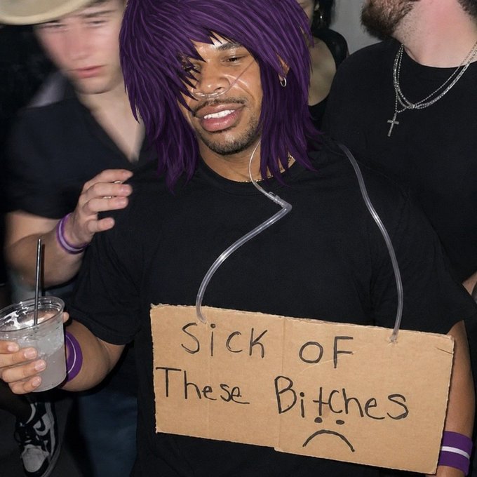 The image features a man with purple hair wearing a black shirt, holding a sign that says "Sick of These Bitches", which has a sad face drawn on it. The background shows other people present at an event or gathering.