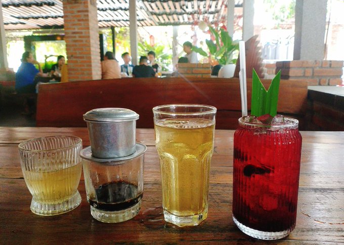 The image features a wooden table with four glasses of different colored drinks, including beer, wine, and cocktails. The glasses are arranged in a line, showcasing various types of beverages for people to enjoy. The scene takes place at a restaurant or bar setting where patrons can relax and socialize while sipping on their chosen drink.