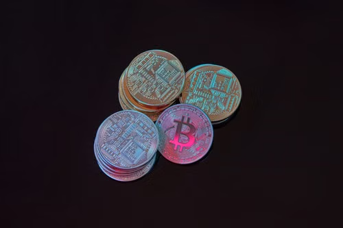 Bitcoin coins with neon-lit circuit designs sit on a dark surface, echoing the post's theme of an insatiable nighttime check on crypto charts and prices despite promising to look just once before bed.