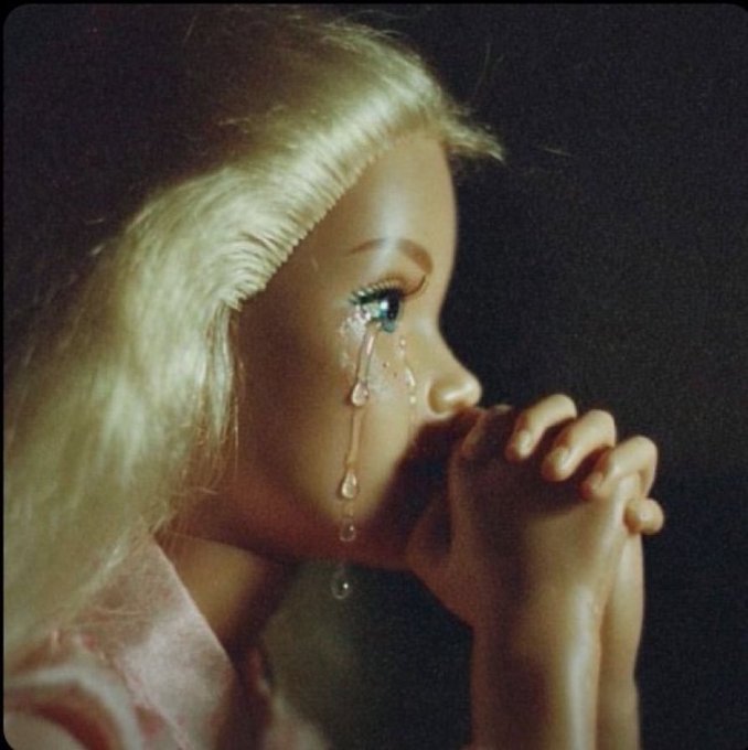 A vintage photograph of a blonde woman in profile with hands clasped in prayer, featuring a tear made of crystal or glass droplets running down her cheek.