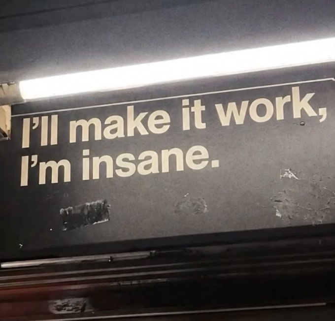 A weathered sign with the text 'I'll make it work, I'm insane.' illuminated by an overhead light.