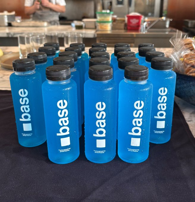 Multiple blue plastic water bottles branded with the word 'base' are arranged in rows on a black table.
