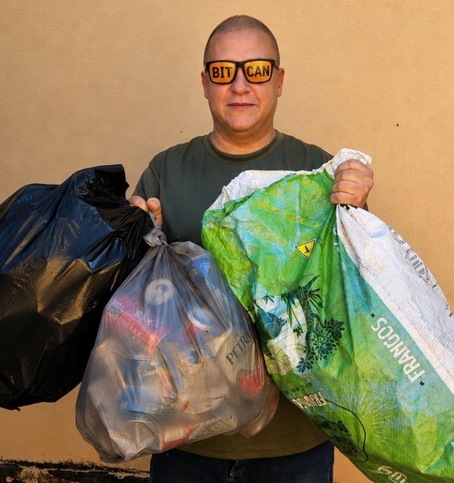 A man wearing 'BITCAN' sunglasses holding several bags filled with recyclable materials against a beige wall.