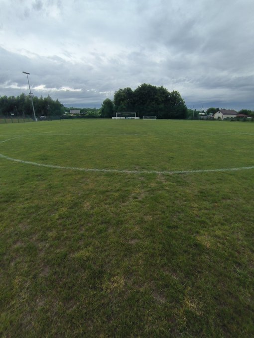 The image shows a large soccer field with a white line down the middle of the green grass. The perspective suggests that the photo was taken from inside or near the field, possibly by someone who has just finished watching a game or is about to start one. The caption on the image reads "instead of looking at your red portfolios every  3 minutes, go outside and touch some grass i'm happy even though we lost 2:1". This message encourages people to engage in outdoor activities like playing soccer as an alternative to spending time on their electronic devices or work-related tasks.