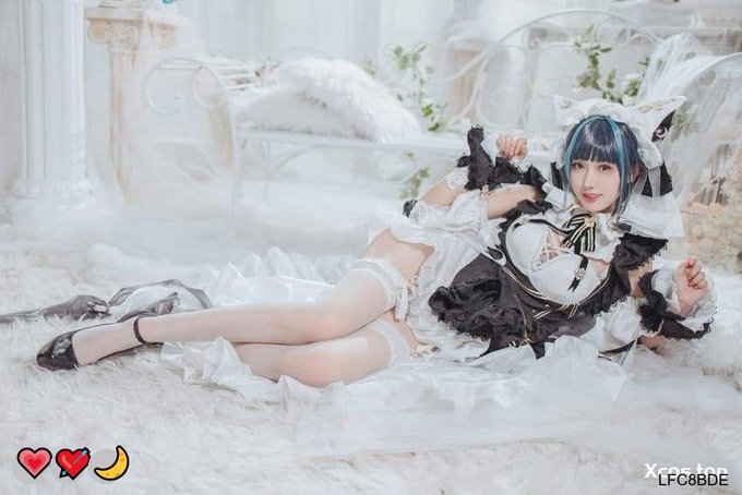 A cosplay photo of a person in a black and white maid outfit with cat ears posing on a fluffy white rug in an ornate bedroom setting, with a code 'LFG88DE' visible.