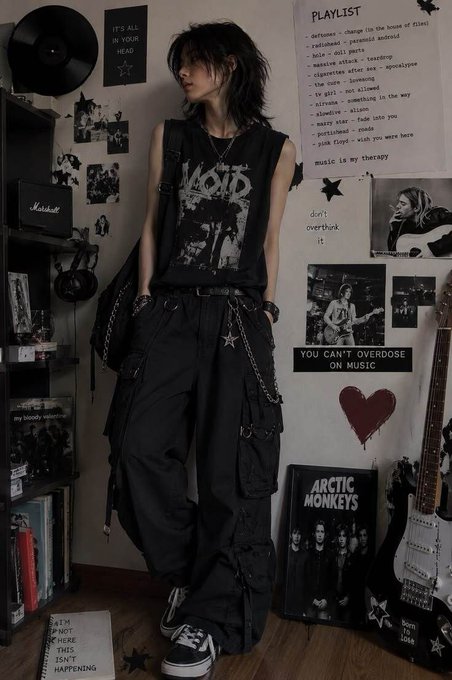 A person with a dark, grunge aesthetic stands in a room wearing a black 'VOID' tank top and black cargo pants with chains, surrounded by music posters, a handwritten playlist, an Arctic Monkeys poster, and a guitar.
