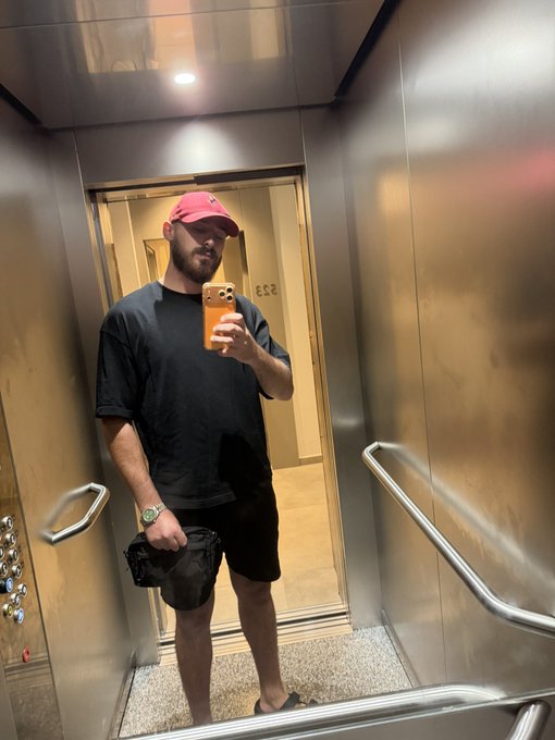 A man in a red hat and black outfit takes a mirror selfie in an elevator, presumably in Dubai as per the post. The number 253 is visible on a door in the background.